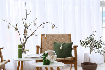 Vase with tree branches, Easter eggs, candles and magazines on table in room