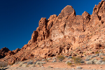 Obraz premium A striking image of reddish rock formations against a beautifully clear blue sky presents the timeless beauty of desert landscapes, capturing their unique geological features.