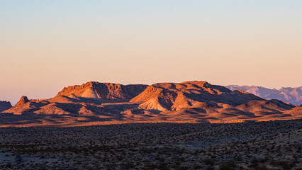 Naklejka premium A stunning view of a desert mountain range at dawn, showcasing warm colors as the sun rises, creating a dramatic contrast with the arid landscape.