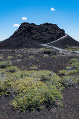 A rugged volcanic landscape displaying dark rocky formations and a winding path leading through...
