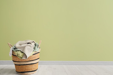 Laundry basket with dirty clothes near green wall