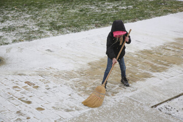 Little girl cleaning snow with broom	