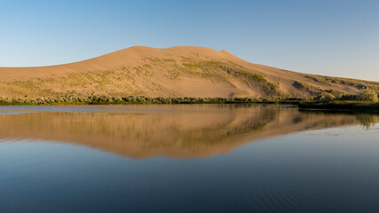 A serene image showcasing a sandy dune with lush greenery reflecting in calm waters, emphasizing the beauty of nature and its peaceful coexistence.