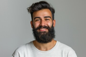 Fototapeta premium Smiling Middle-Eastern man with a stylish beard and friendly expression against a neutral background.