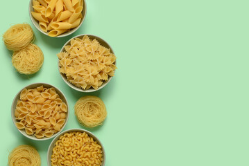 Bowls with different tasty uncooked pasta on green background