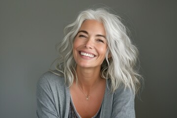 Fototapeta premium Smiling middle-aged woman with curly gray hair, wearing a cozy gray sweater against a neutral backdrop.
