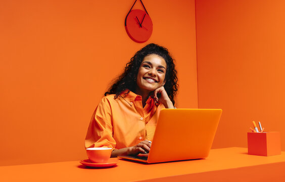 Female working from home on laptop, smiling in monochromatic minimalist office setup