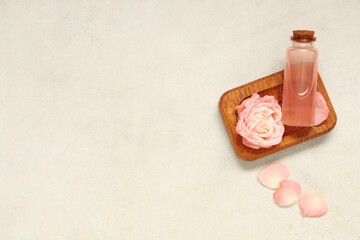 Composition with bottle of cosmetic oil, wooden tray, petals and rose on beige background