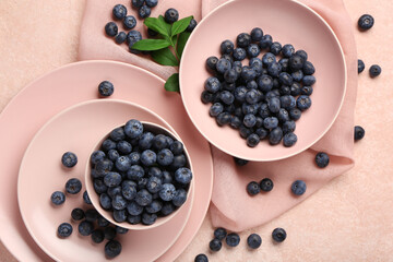 Bowl and plate with sweet fresh blueberries on pink background