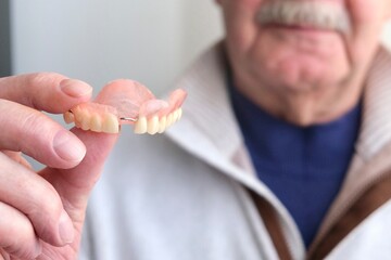 An elderly man holds a denture in his hands. The concept of stomatology and prosthetics. A dental prosthesis. Dentures on hooks