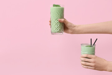 Female hands with glasses of fresh spinach smoothie on pink background