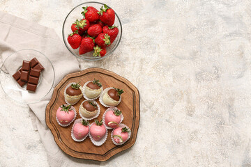 Wooden board with chocolate covered strawberries and glass bowl of fresh berries on grey background