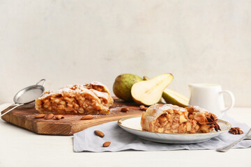 Plate and wooden board with pieces of tasty pear strudel on light background