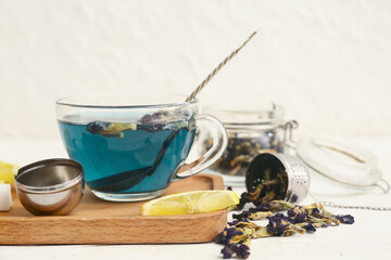Cup of butterfly pea flower tea on wooden tray and tea strainer with dried flowers on table, closeup