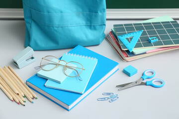 School backpack with different stationery supplies and eyeglasses on white table