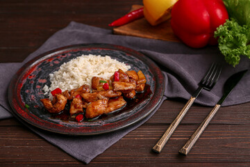 Tasty sweet and sour chicken in plate with rice on black wooden table