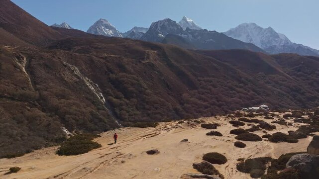 Mountain climber ascending barren Himalayan valley, snow capped Everest looming above rugged Nepalese terrain, embodying wilderness solitude