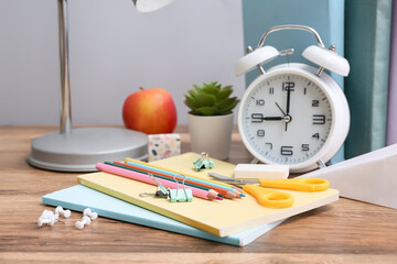 set of different stationery with alarm clock on wooden table against grey wall