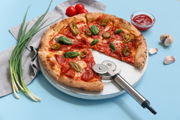 Composition with tasty pizza, ingredients and cutter on blue background