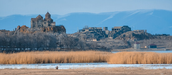 Monastery on the lake shore. Churches on the river bank. Winter landscape with church and lake. Monastery in nature. Frozen lake and rocky mountains