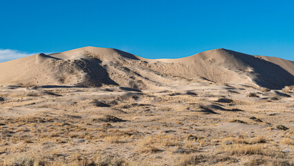An expansive view of sandy dunes illuminated by the bright blue sky, emphasizing the simplicity and beauty of the natural desert landscape, inviting exploration.