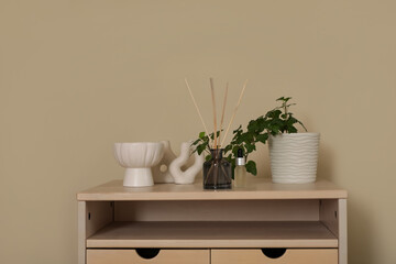 Aroma reed diffuser with essential oil, decor and houseplant on chest of drawers in room. Closeup