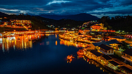 Fototapeta premium Baan Rak Thai Village at sunset reflections of houses and restaurants along the lake in Chinese-style architecture with colorful lights line the water. a popular tourist attraction in Mae Hong Son
