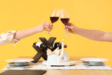 Young couple with wine at restaurant table on yellow background