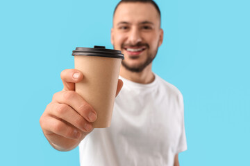 Young man with paper cup of coffee on blue background