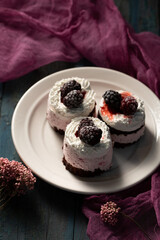 Delicious cream cakes with frozen blackberries on a white plate, top view