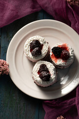 Delicious cream cakes with blackberries on a white plate, top view