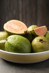 Fresh whole and cut guava fruits in bowl on grey textured table, closeup