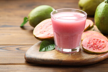 Tasty guava juice in glass, leaves and fruits on wooden table, closeup