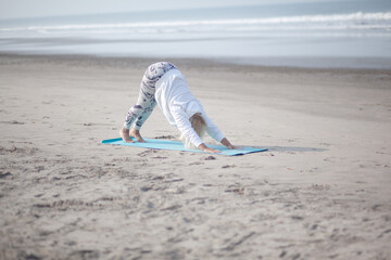 Middle-aged woman does yoga on the shore of the Indian Ocean early in the morning