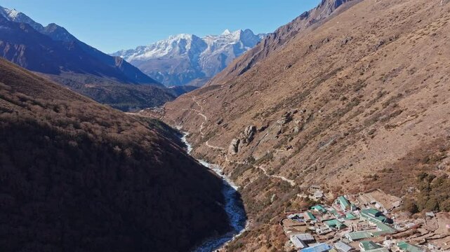 Towering Everest peaks rising above serpentine river winding through Nepalese valley, revealing sparse vegetation and mountain settlement of Shomare