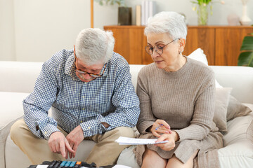 Middle aged senior couple sit with laptop and paper document. Older mature man woman reading paper...
