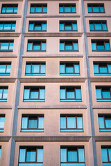 Modern building facade with a repetitive pattern of blue-tinted windows, creating a geometric and symmetrical urban design.