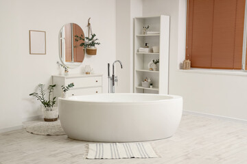 Interior of light bathroom with eucalyptus branches, bathtub and shelf unit