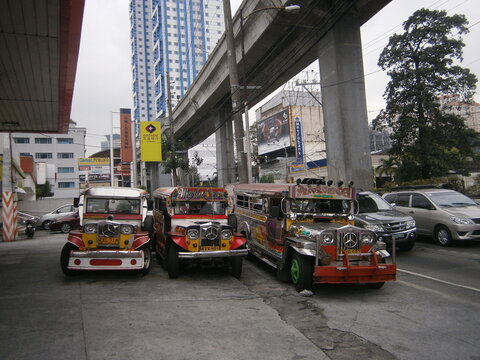 Mercedes jeepneys parked by the main freeway with the metro train flyover overhead. Dec 2014. Quezon City, Metro Manila. Philippines