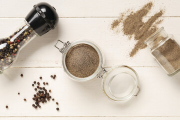 Jars with black pepper powder and peppercorns on white wooden background