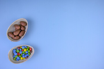 Easter composition with chocolate eggs and colored candies in halves of chocolate eggs on a blue background.