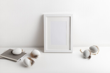 Frame mockup with decorative easter eggs in natural colours and notepad on the white table. Happy Easter concept, copy space for your text.