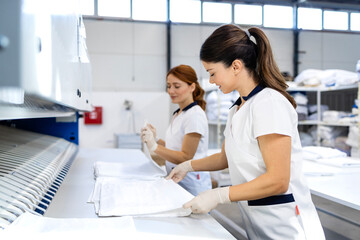 Female laundry workers folding linen and bedsheets after ironing in dry cleaning service.