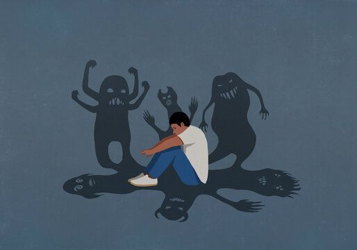 Shadows of monsters surrounding anxious teenage boy hugging knees

