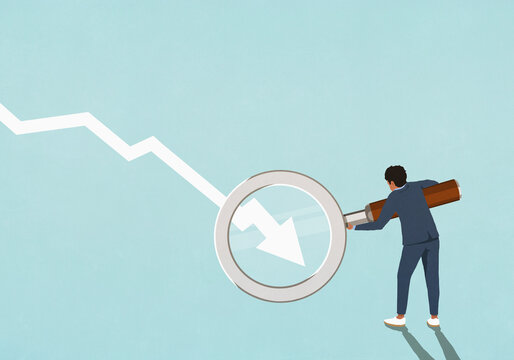 Businessman holding magnifying glass over descending chart arrow
