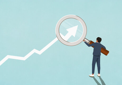 Businessman holding magnifying glass over ascending chart arrow
