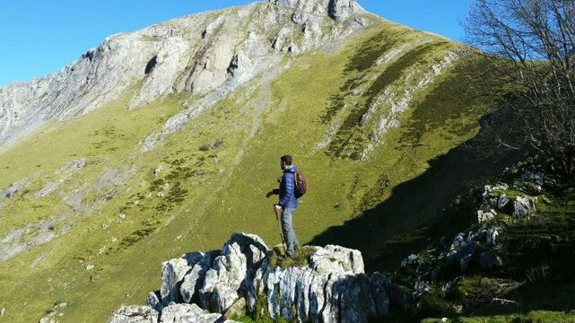 Solo hiker observing majestic mount txindoki landscape from limestone rock formation in gipuzkoa. Green slopes and dramatic cliff faces under blue sky