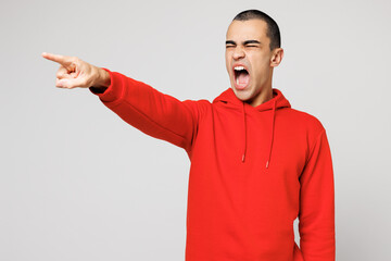Fototapeta premium Young dissatisfied furious outraged sad middle eastern man he wear red hoody casual clothes point index finger aside scream isolated on plain solid white background studio portrait. Lifestyle concept.