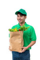 Asian male grocery delivery worker in green uniform holding paper bag filled with fresh vegetables isolated on white background