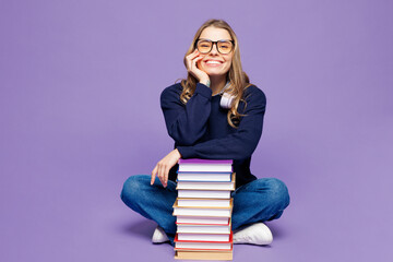 Full body young happy girl student wear blue casual clothes glasses headphones sitting hold stack...